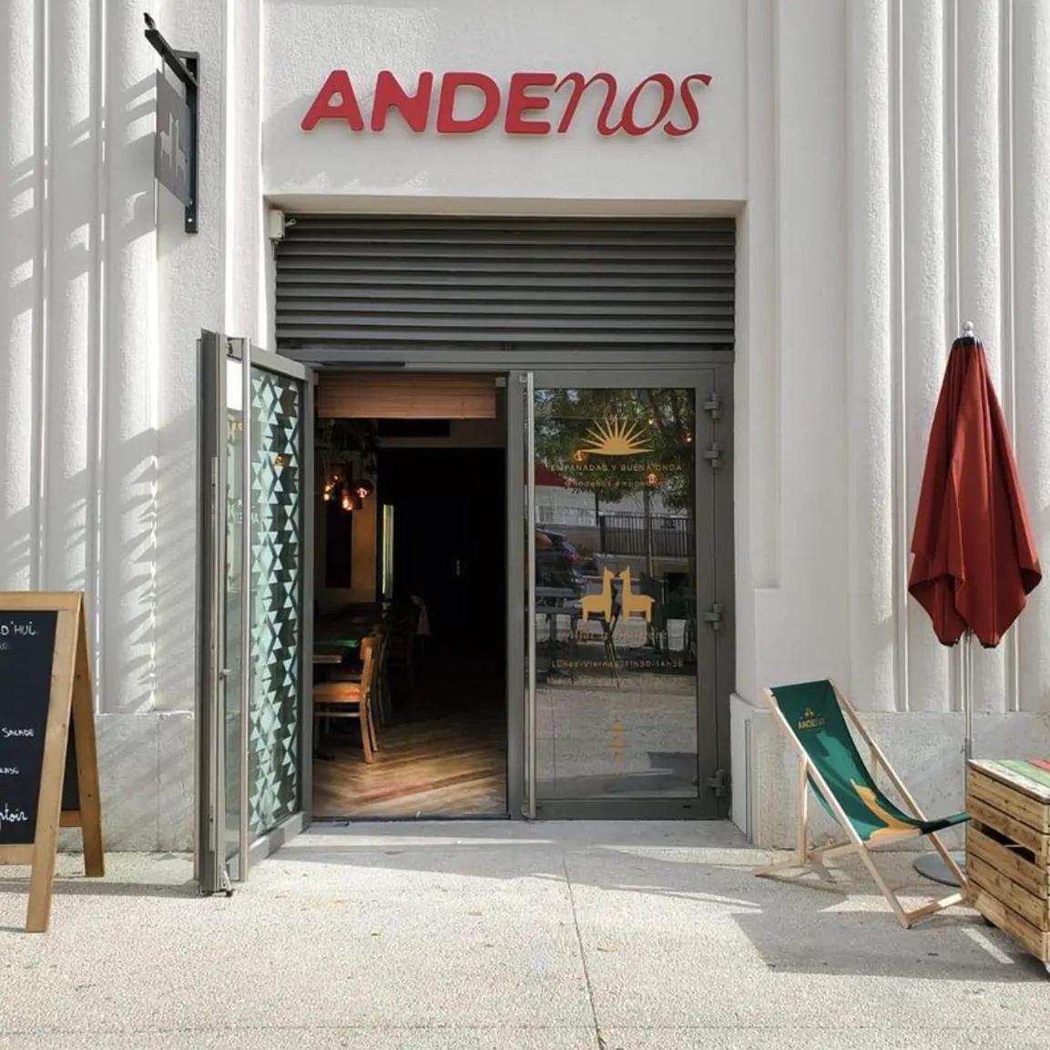 La devanture d’Andenos : l’enseigne rouge sur la façade blanche, la porte vitrée ornée de deux lamas et de l’inscription « Empanadas y Buena Onda », un transat vert et un parasol rouge.