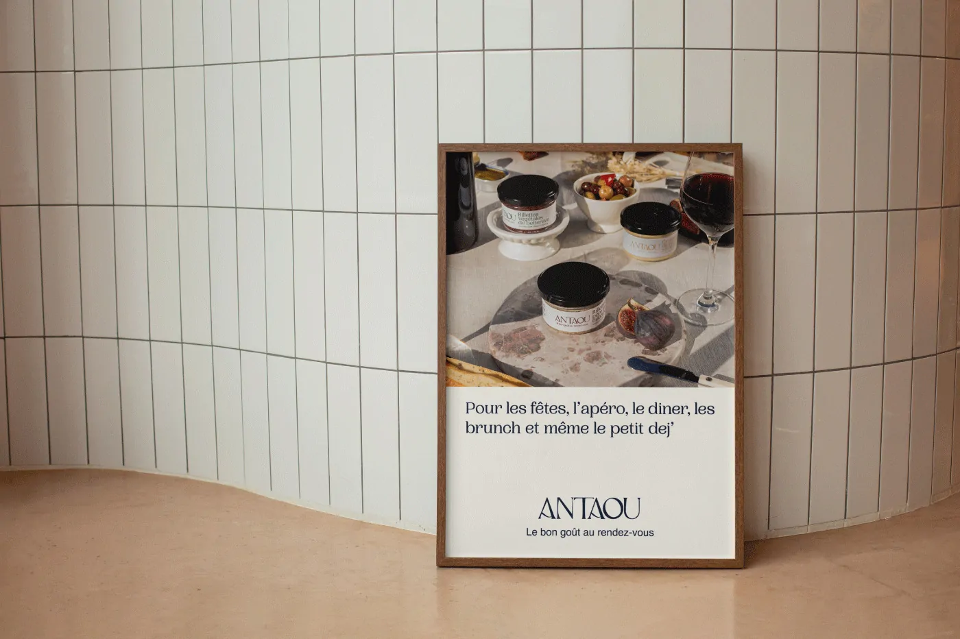 Une affiche encadrée contre un mur de carreaux blancs : une photo de table et le logo Antaou.