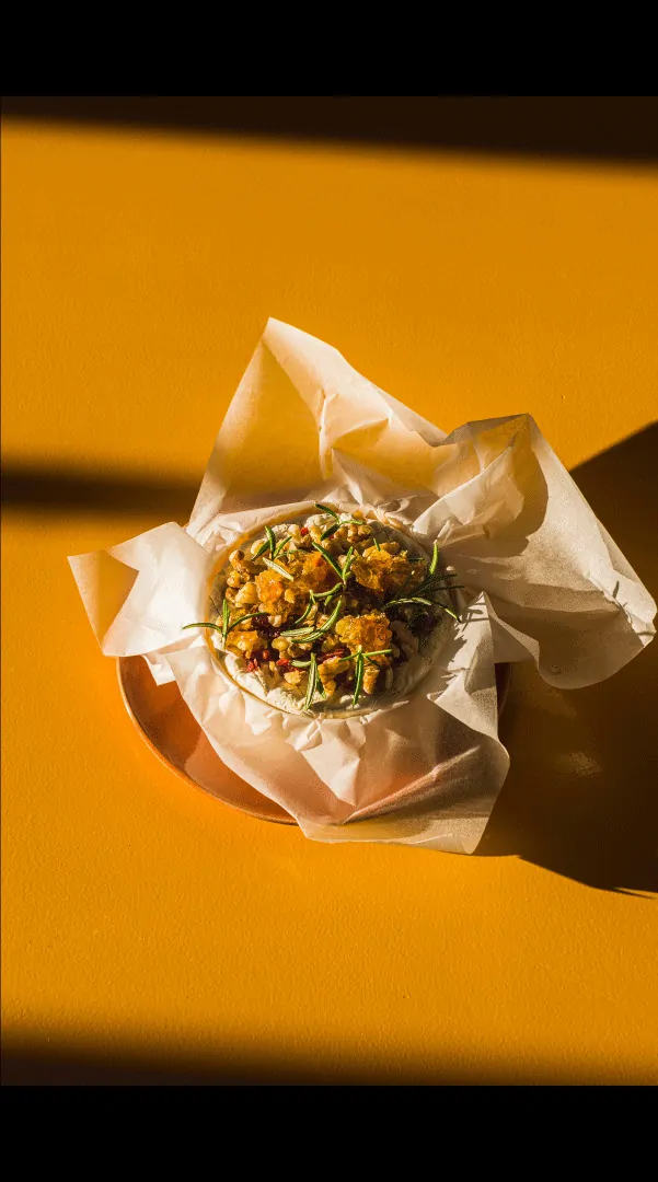 Une portion de focaccia garnie dans un papier, sur un fond jaune vif.