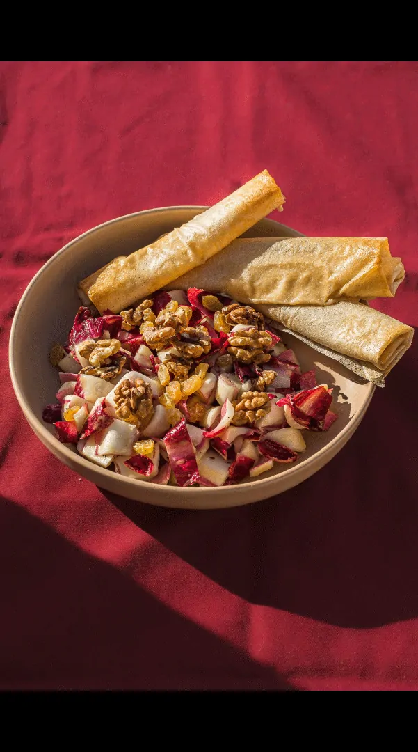 Un bol de salade de légumes et de fromage avec des gressins, sur une nappe rouge.