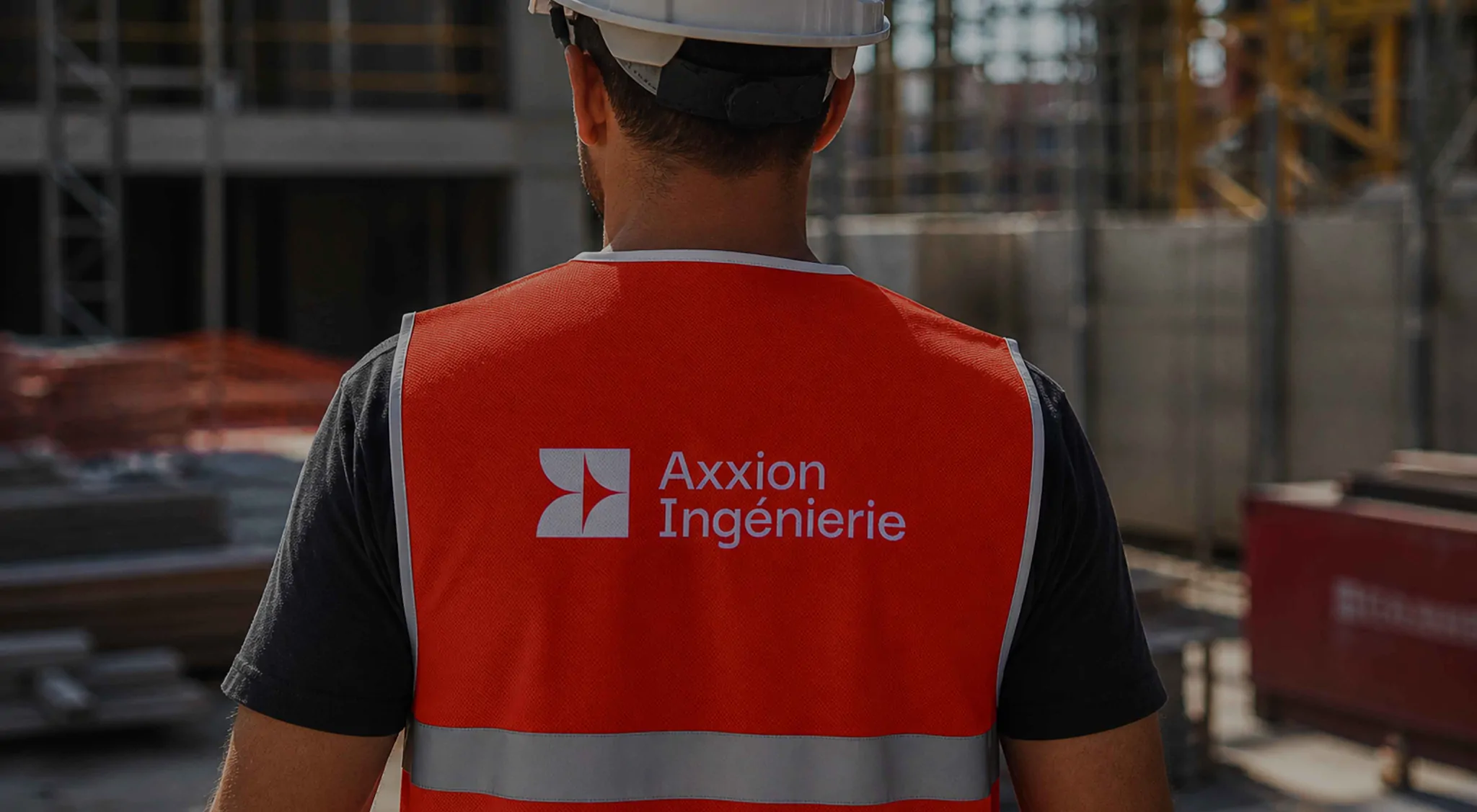 Un ouvrier de dos, en gilet orange portant le logo Axxion Ingénierie, devant un chantier (image générée par IA).