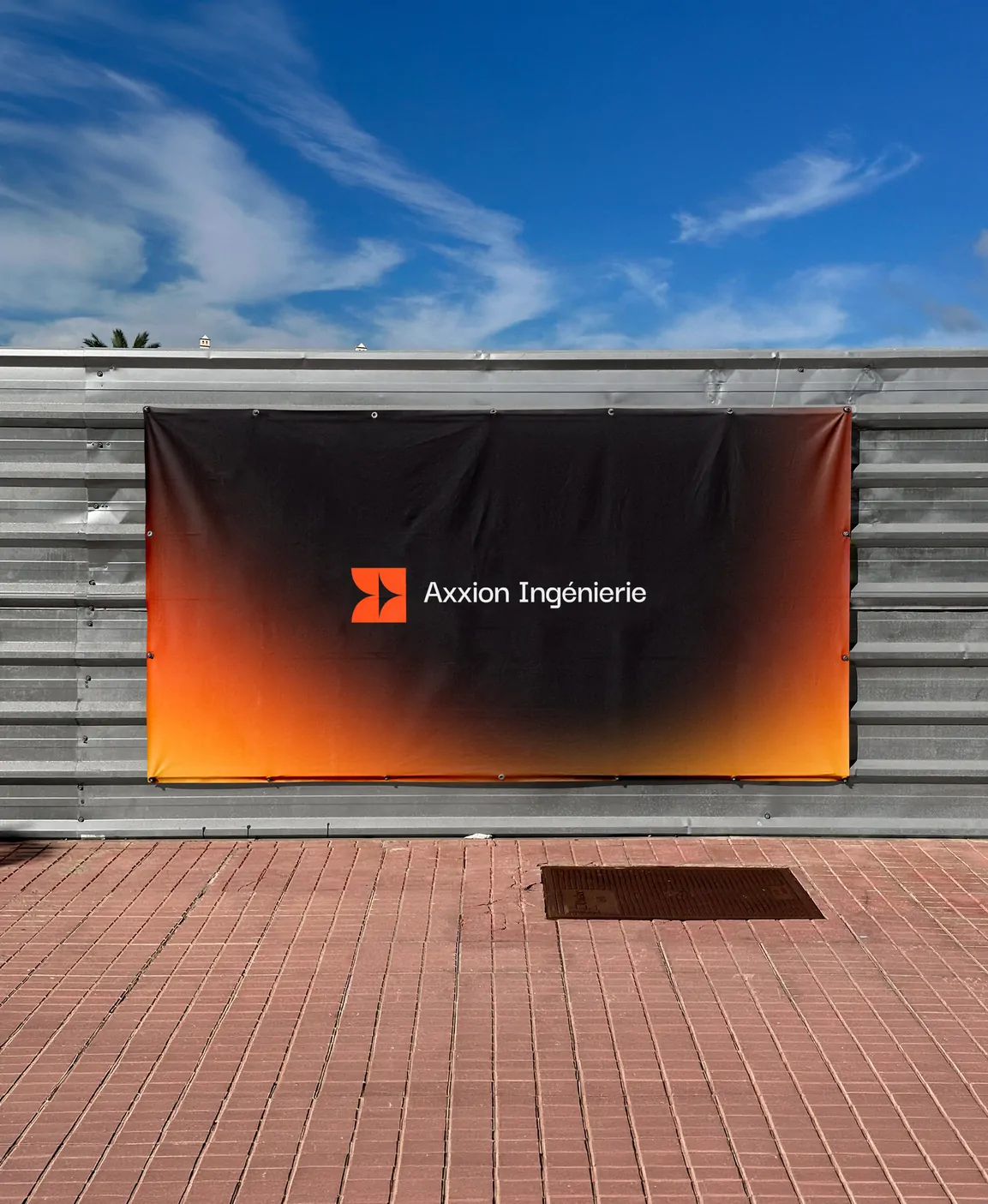 Une grande bâche noire à dégradé orange portant le logo Axxion Ingénierie, tendue sur une palissade de chantier.