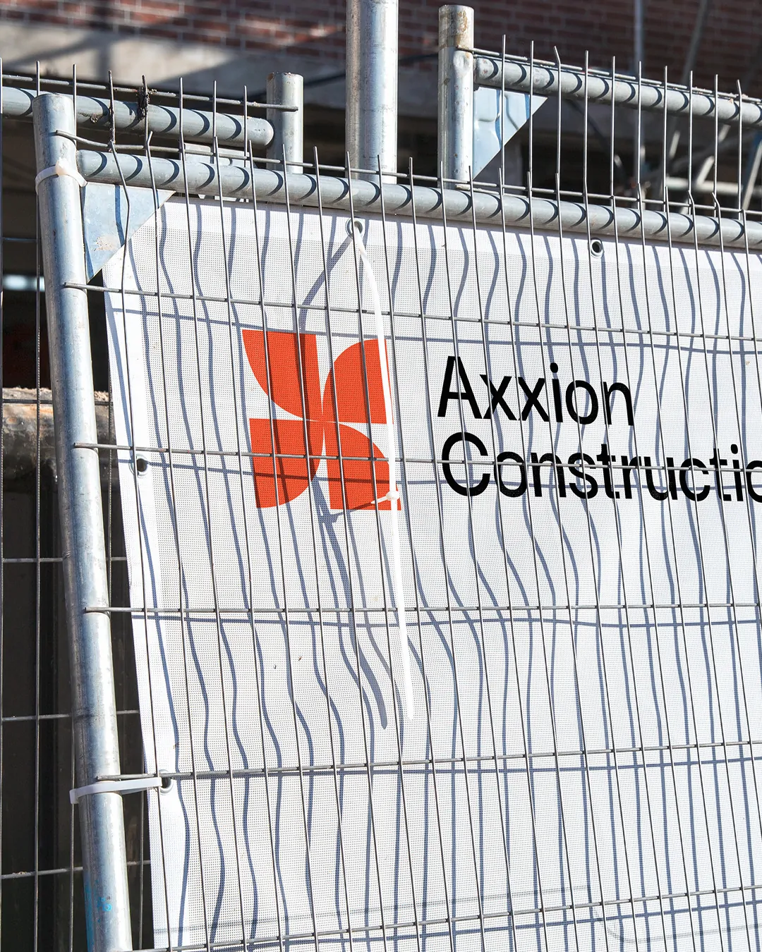 Une bâche blanche à motif de vagues grises, logo Axxion Construction, attachée à une grille de chantier.