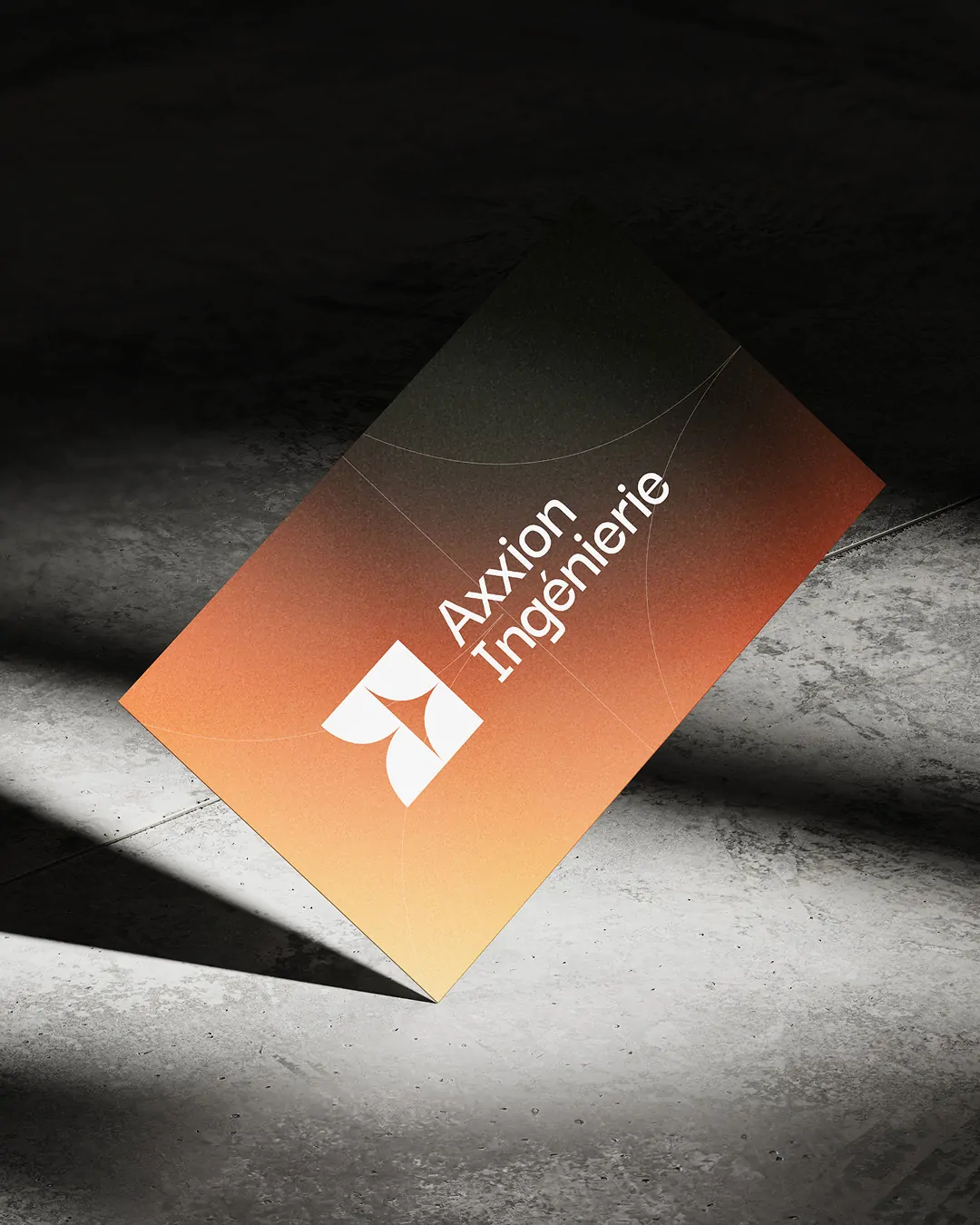 Une carte de visite au dégradé orange et noir, posée en biais sur du béton, dans un faisceau de lumière.