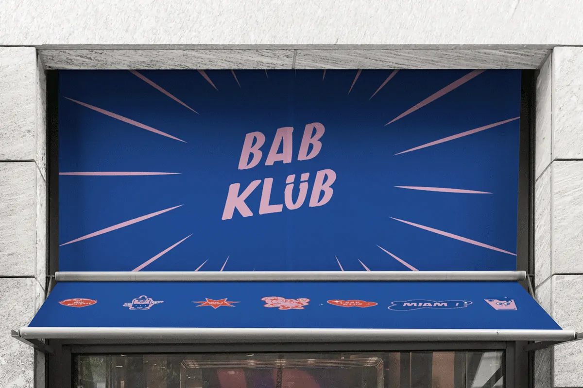 Le store d’une devanture de commerce imprimé du logo « Bab Klüb » en rose sur fond bleu.