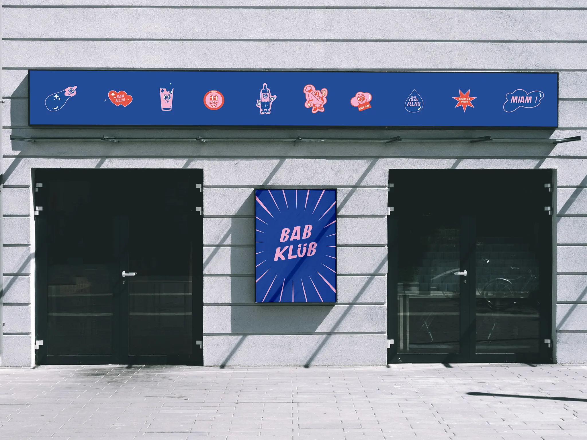 Une façade grise : une enseigne bleue ornée d’autocollants et un panneau carré « Bab Klüb » entre deux vitrines noires.