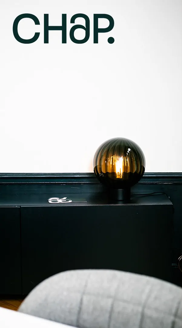 Une lampe-globe posée sur un meuble noir marqué du monogramme, sous la signature « CHAP. ».