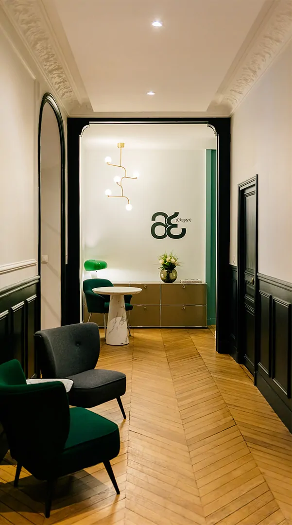 Un couloir parqueté du cabinet, ses moulures et ses boiseries noires, et au fond le monogramme sur le mur blanc.