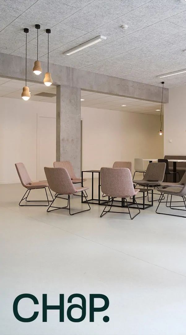 Un espace de réunion lumineux : des fauteuils roses autour de tables hautes, des suspensions, et la signature « CHAP. » en bas à gauche.