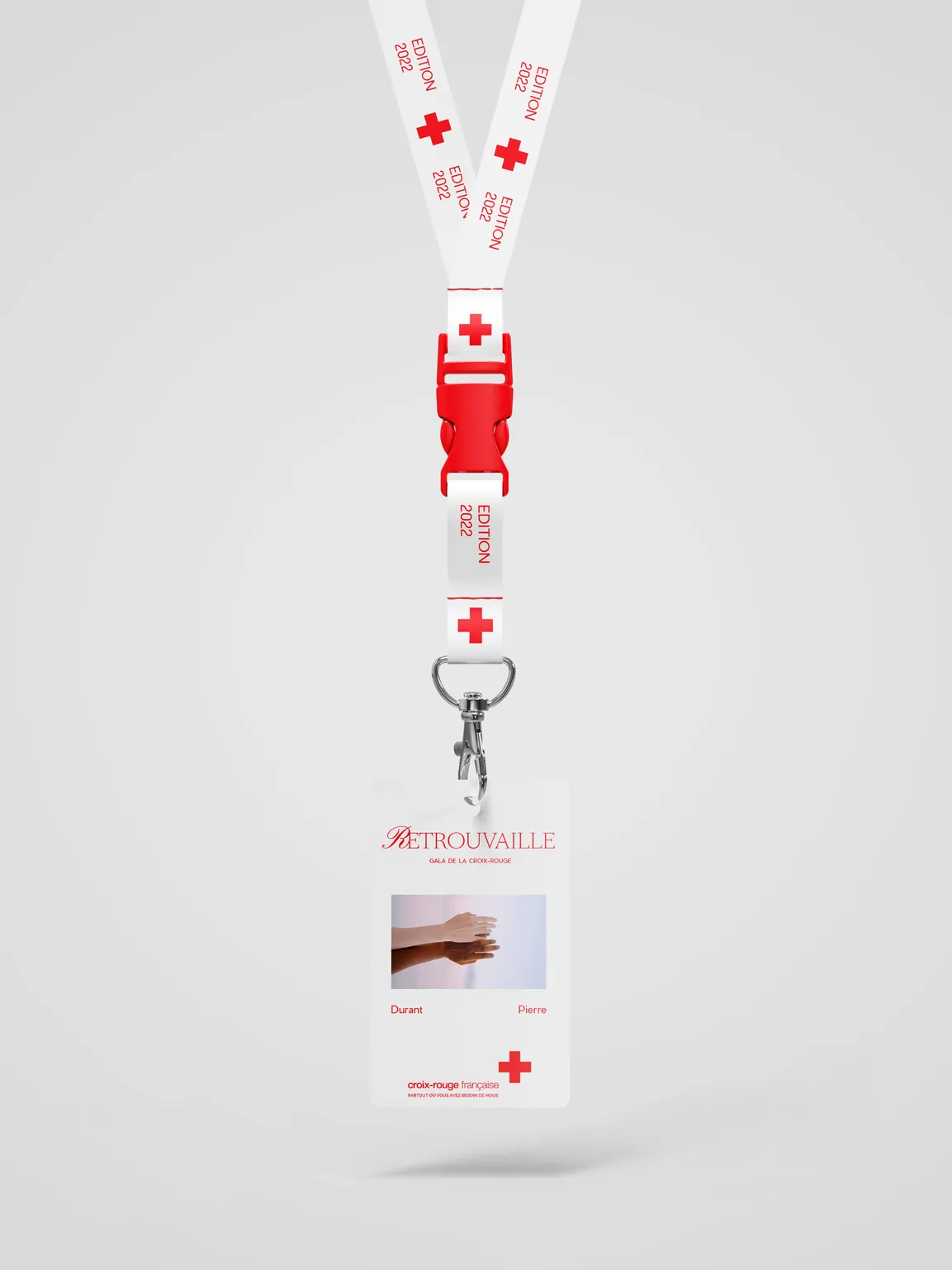 Un badge sur son tour de cou blanc imprimé de croix rouges, la photo de deux mains au recto.