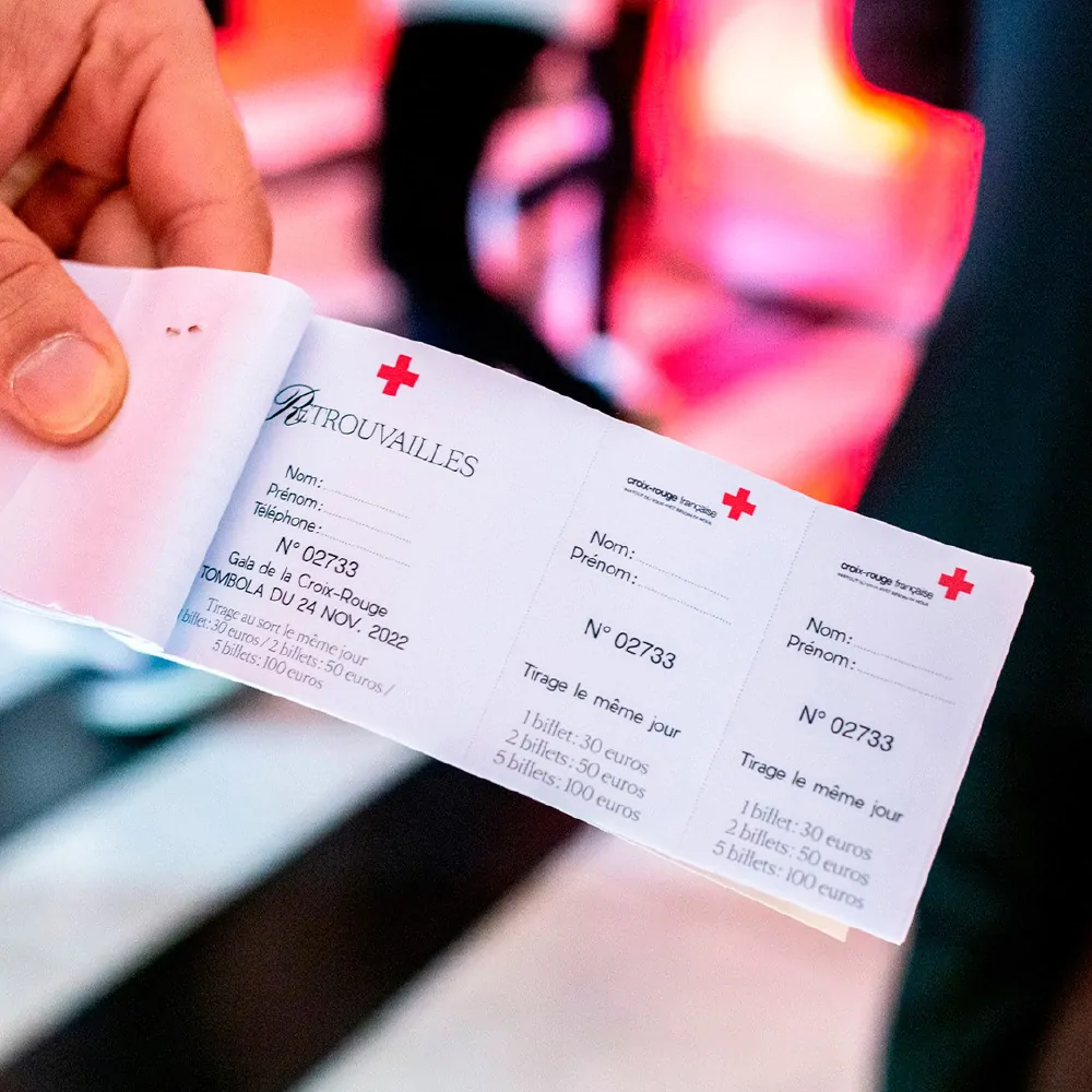 Un billet de tombola tenu à la main, avec les croix rouges et le titre « Retrouvailles ».