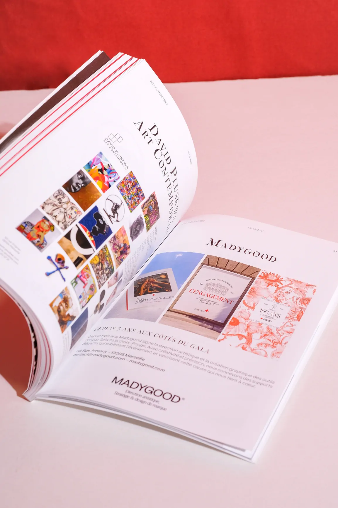 Le catalogue ouvert sur une double page de visuels et de textes, posé sur un fond rouge.