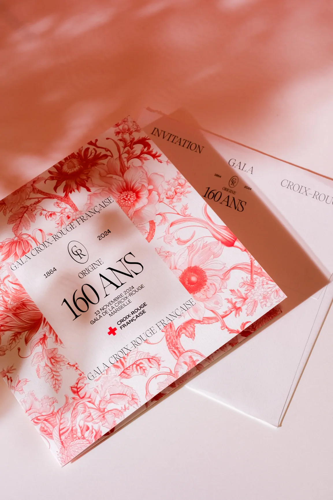 L’invitation et son enveloppe, dans une lumière rose striée d’ombres de feuillages.
