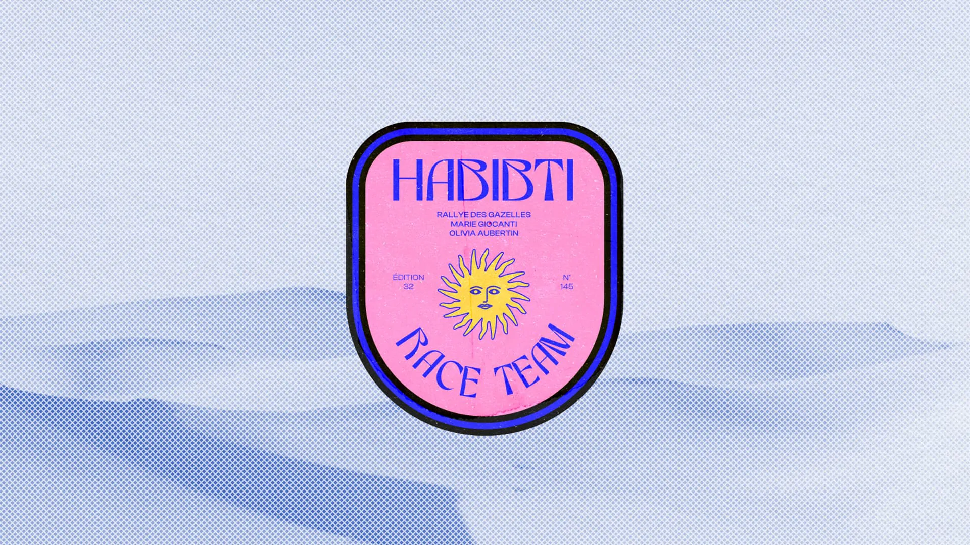 Le badge de Habibti Race Team, un blason rose cerclé de bleu orné d’un soleil, posé sur un décor de dunes pâles.