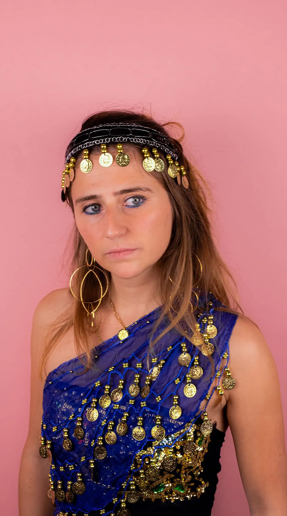 Portrait d’Olivia, le front orné de pièces dorées, sur un fond rose.