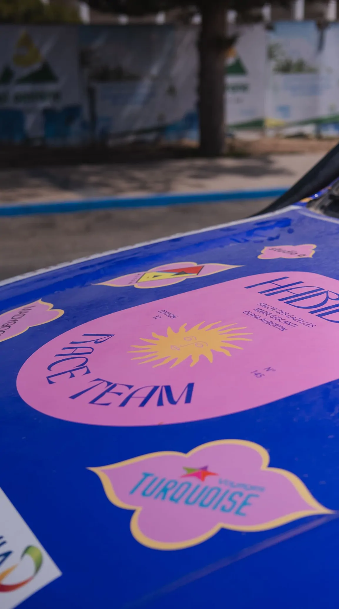 Le capot du 4x4 vu de près : le logotype Habibti Race Team, un soleil rose et un écusson turquoise sur fond bleu.