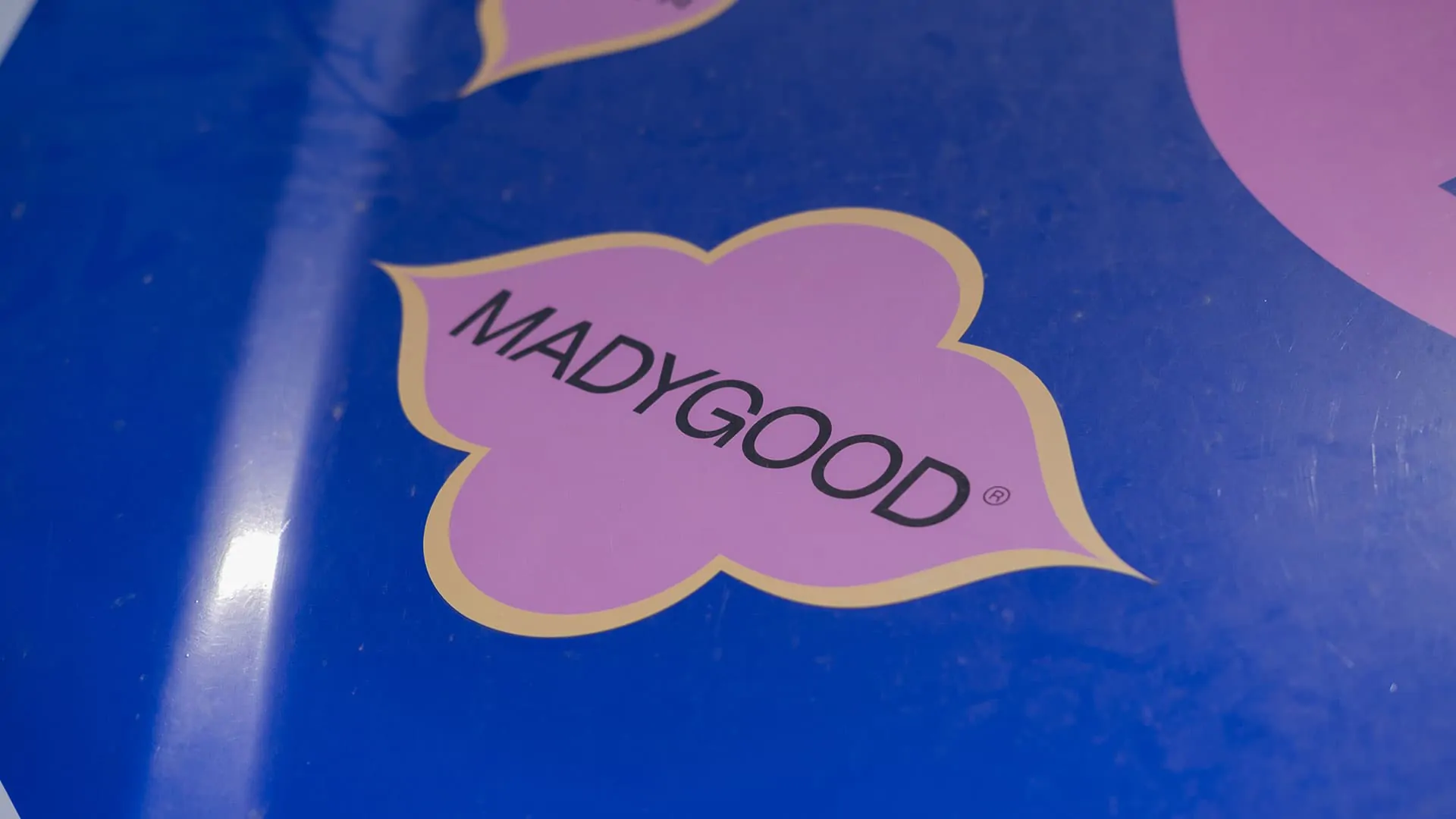 Un écusson « MADYGOOD » en forme de fleur rose sur la carrosserie bleue du véhicule.