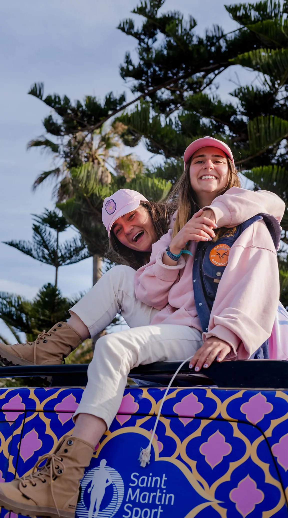 Marie et Olivia, casquettes roses, assises sur le toit du 4x4 aux motifs bleus, à Essaouira.