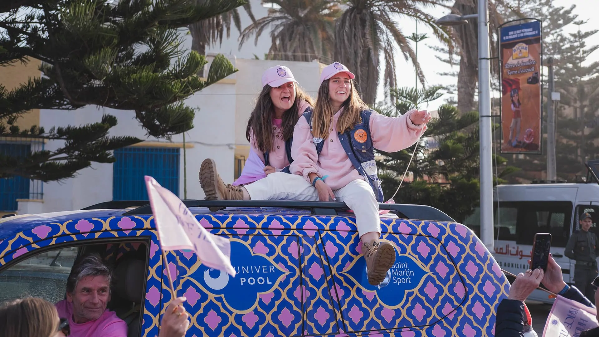 Les deux équipières sur le toit du véhicule à l’arrivée, un drapeau rose à la main.
