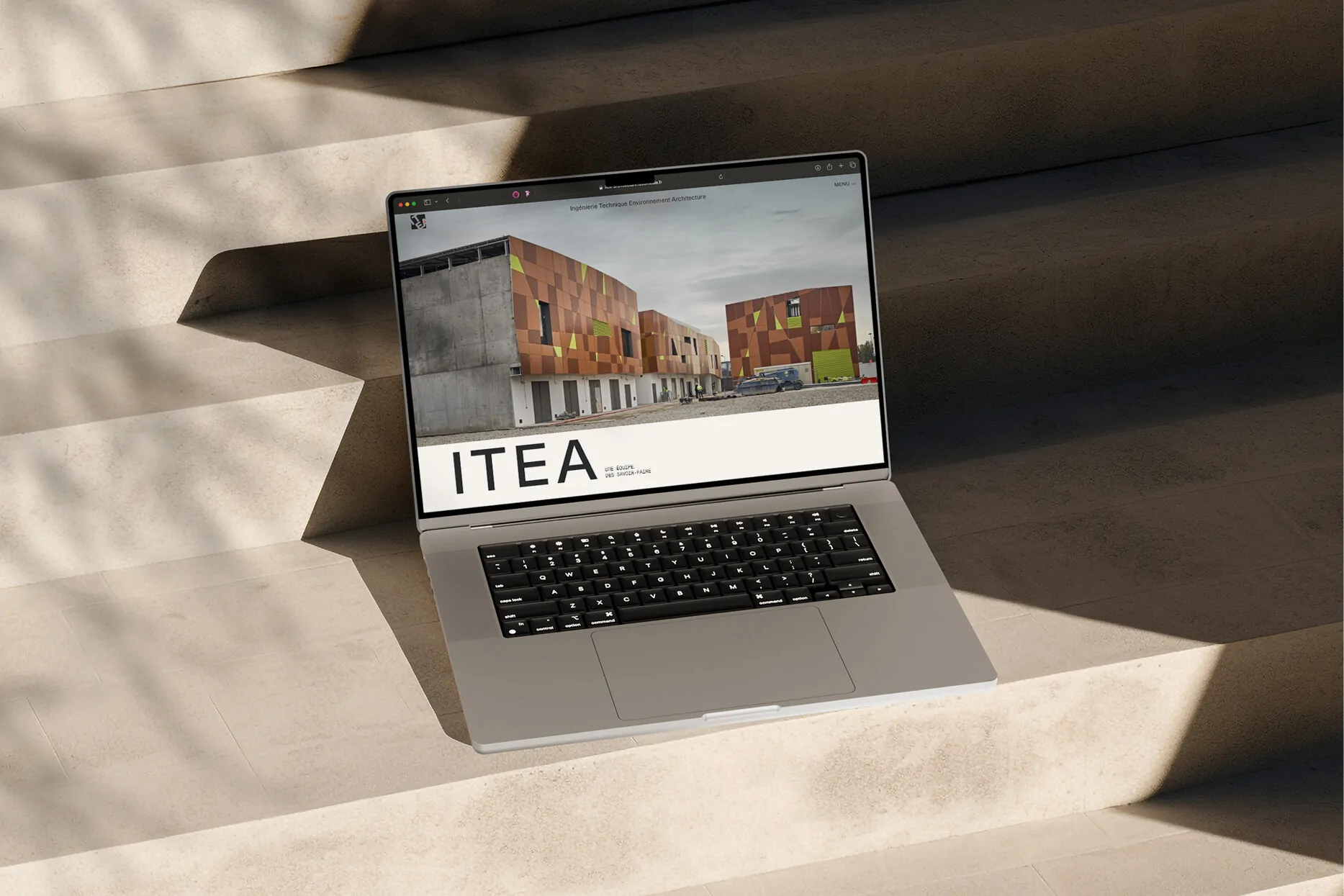 Un ordinateur portable posé sur des marches de pierre, affichant le site d’ITEA et sa façade.