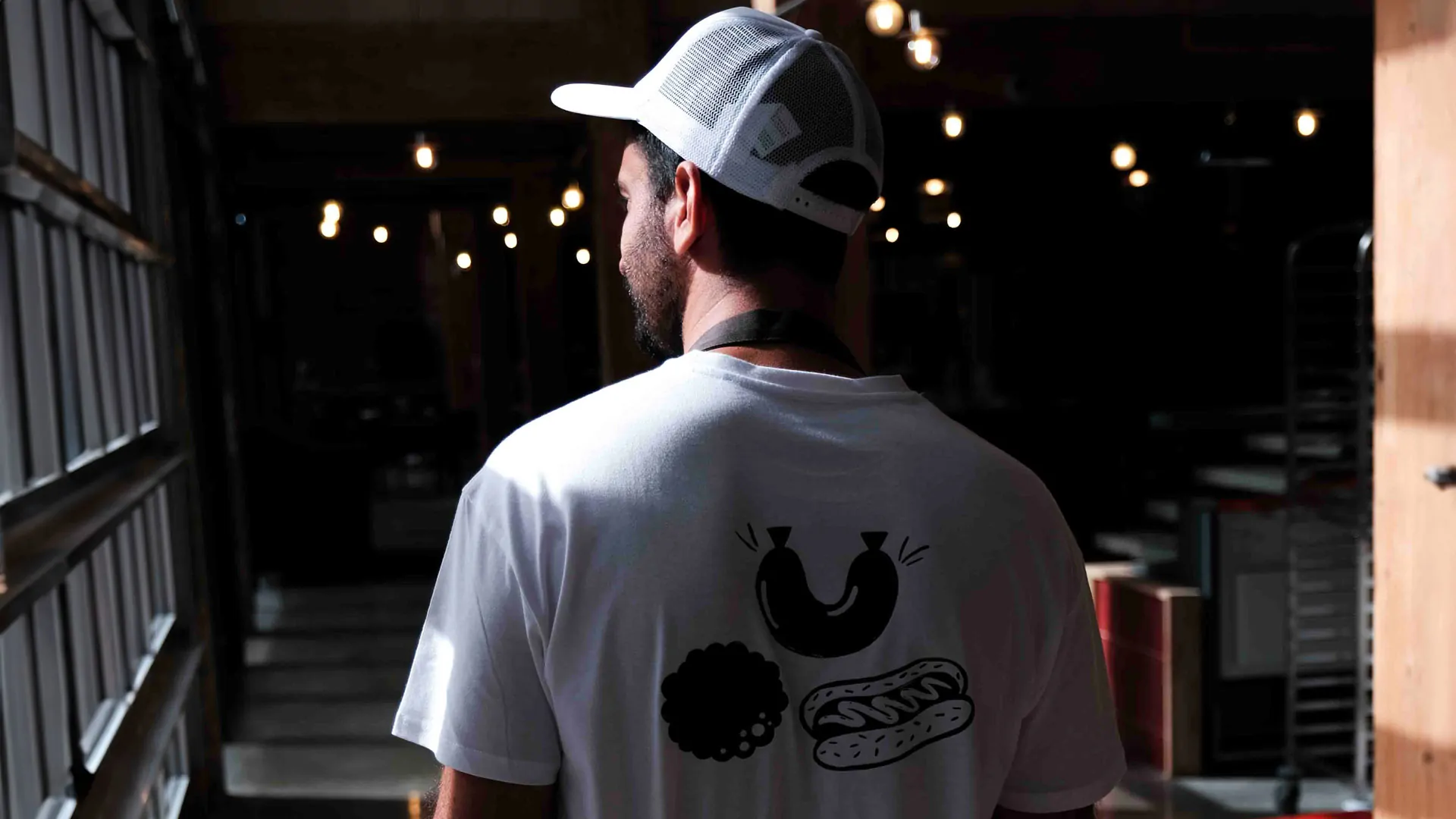 Un membre de l’équipe, de dos, dans le tee-shirt blanc de La Truffe et l’Andouille et une casquette, devant les baies vitrées des Halles de la Cartoucherie.