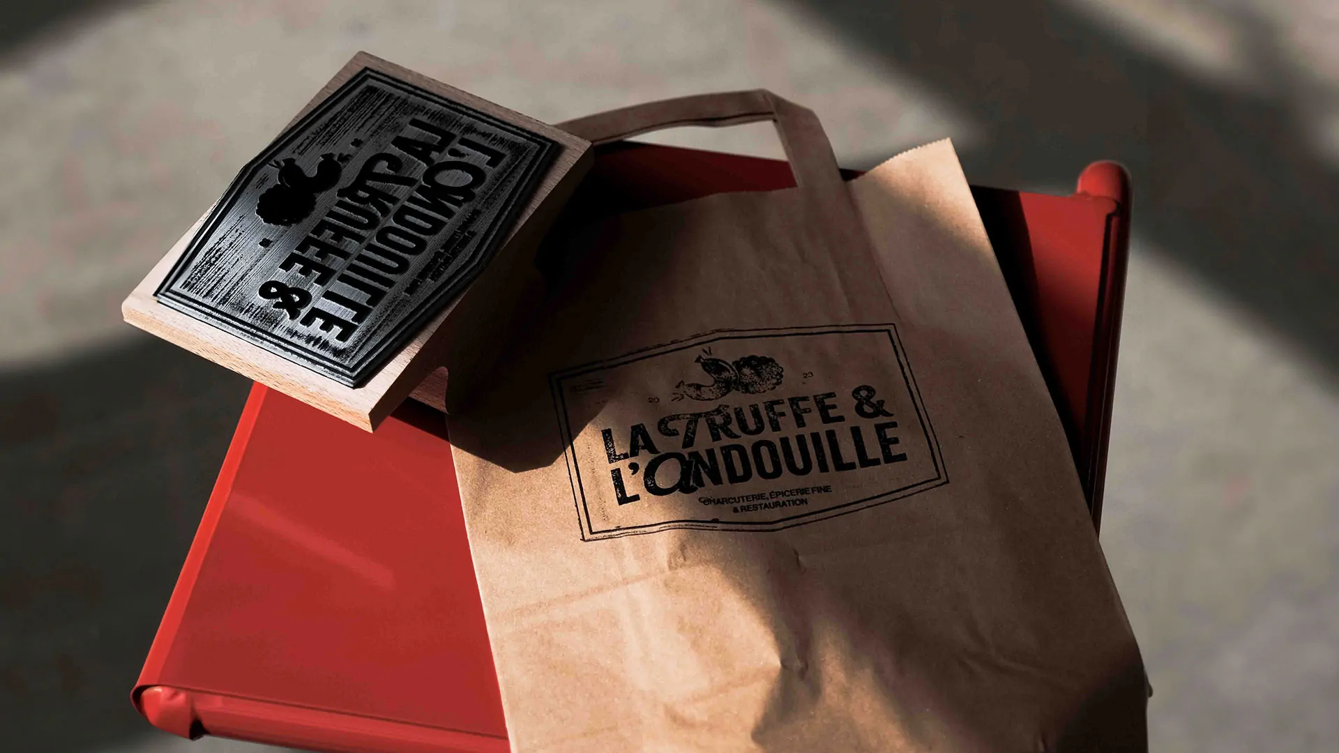 Un sac en papier kraft et un tampon « La Truffe & l’Andouille » posés sur un plateau rouge.