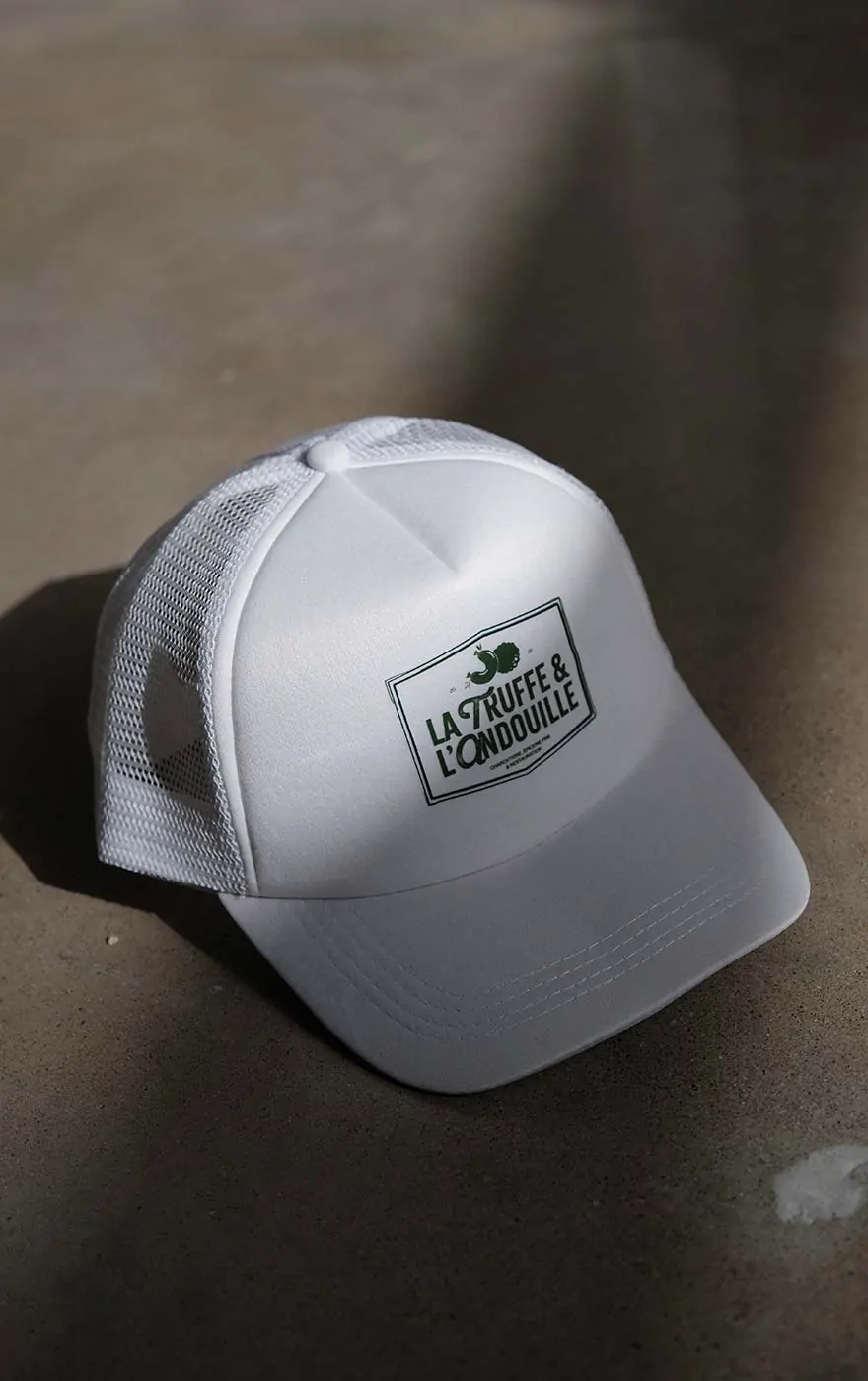 Une casquette blanche portant l’étiquette « La Truffe & l’Andouille ».