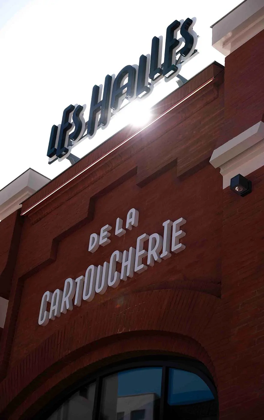La façade en brique des Halles de la Cartoucherie et son enseigne « Les Halles » contre le ciel.