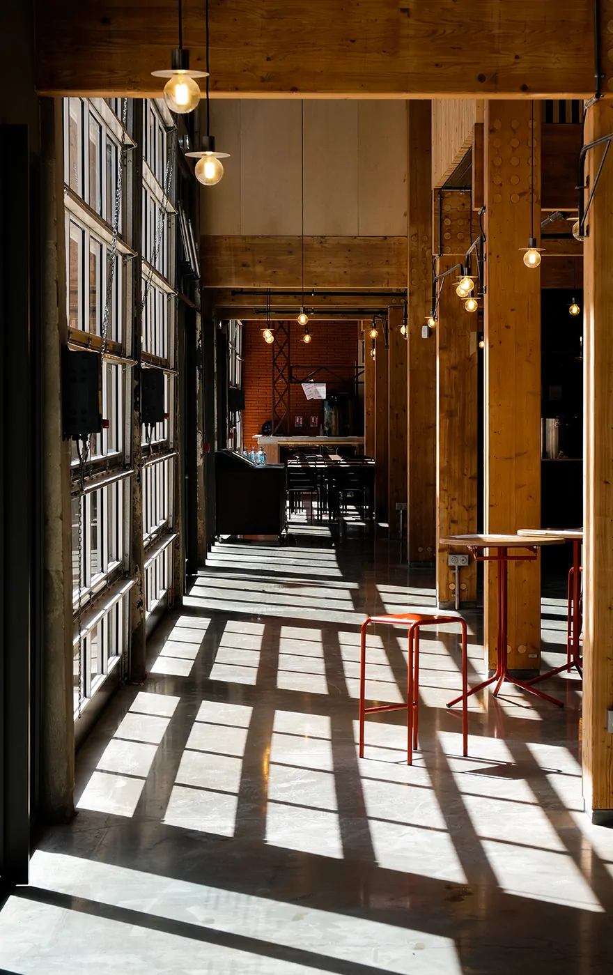 Une allée des Halles baignée de lumière, avec ses baies vitrées et ses tables rouges.