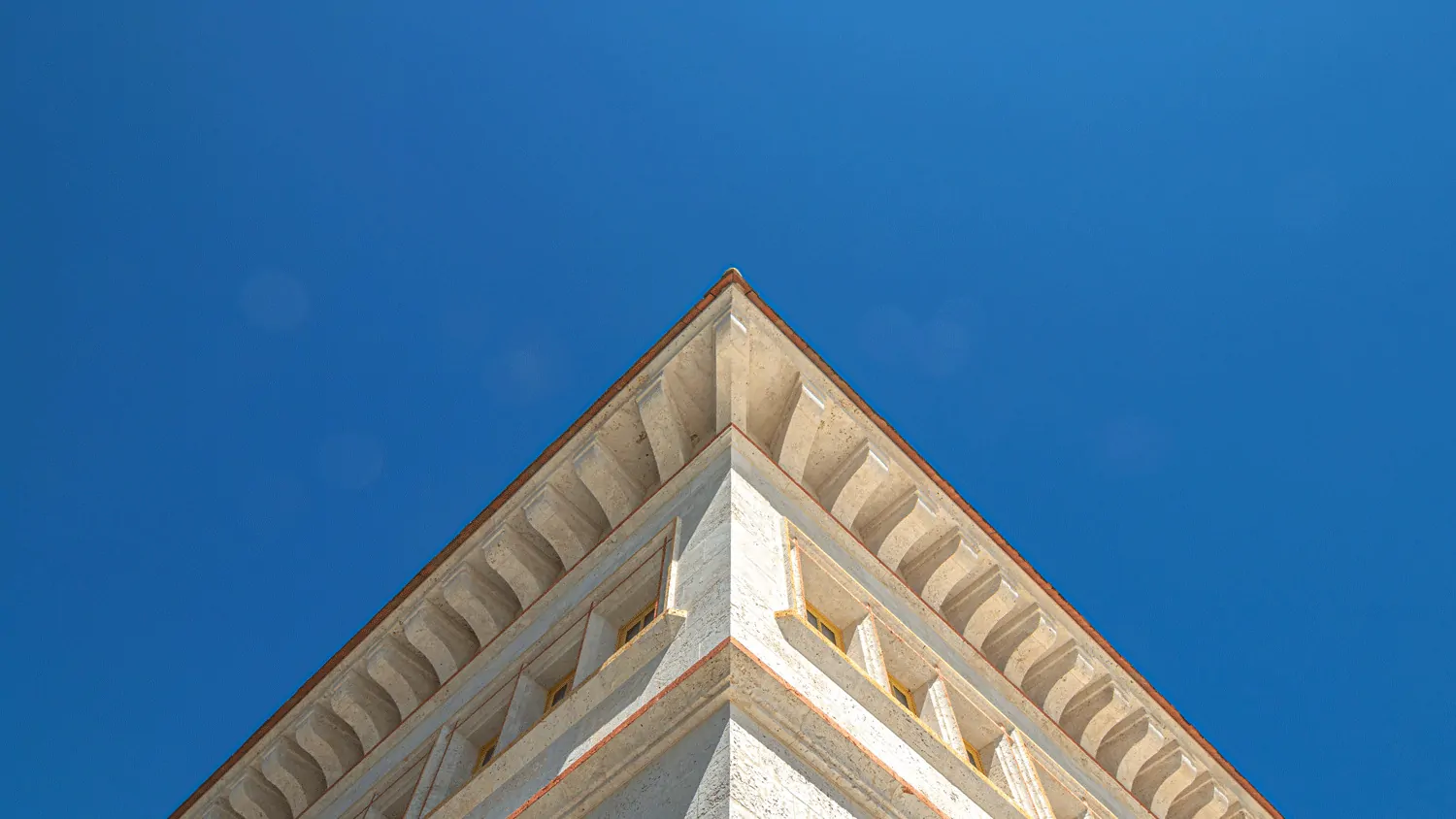 L’angle d’un fronton en pierre blonde contre un ciel bleu profond.