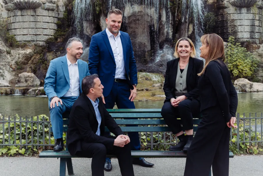 Cinq membres de l’équipe de PCC posés autour d’un banc vert, devant la cascade du parc du Palais Longchamp.
