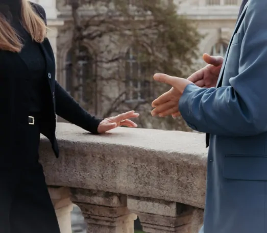 Une femme et un homme discutent en gesticulant, de profil, appuyés à une balustrade de pierre.