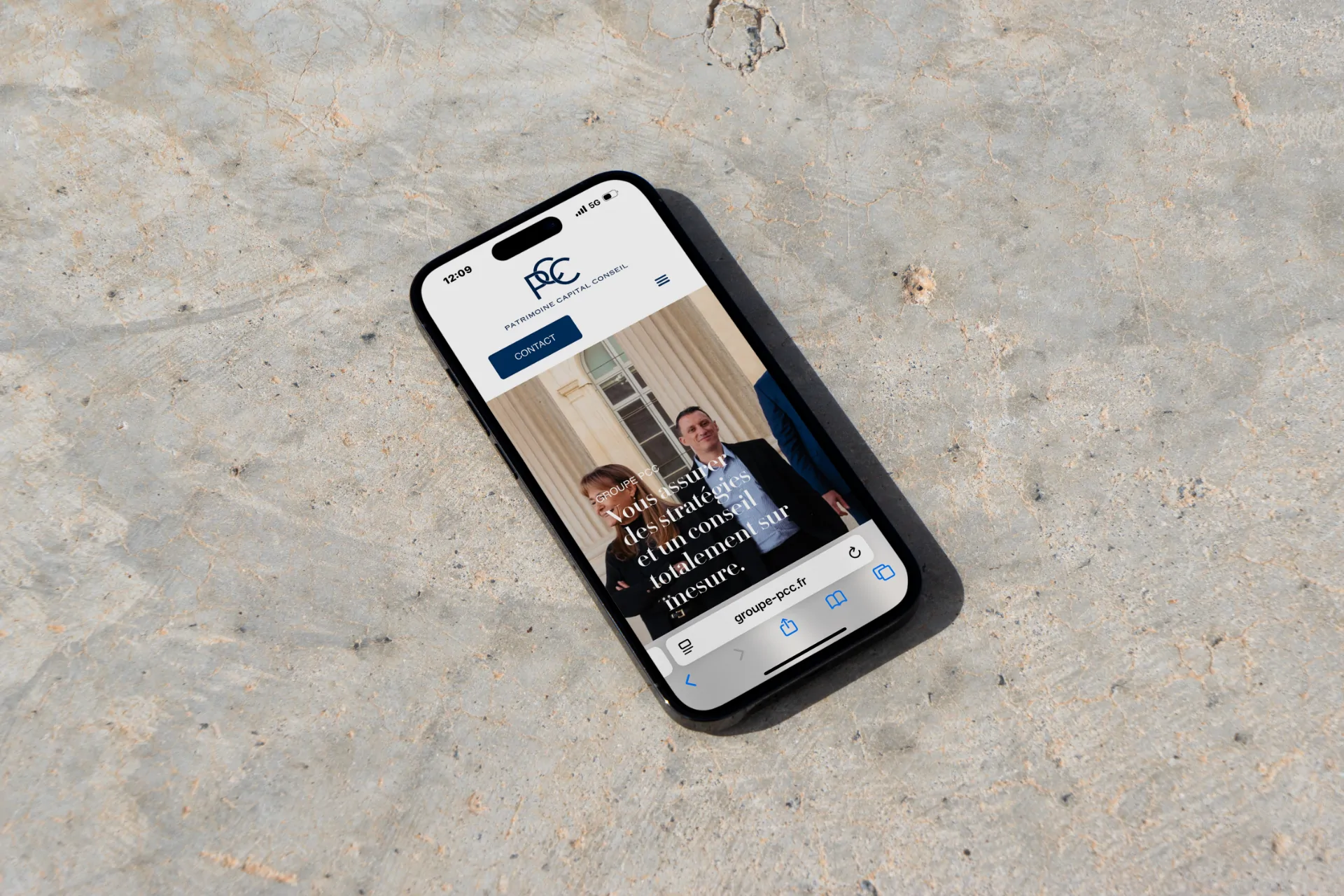 Un téléphone posé sur un sol de pierre, affichant le site de PCC (groupe-pcc.fr).