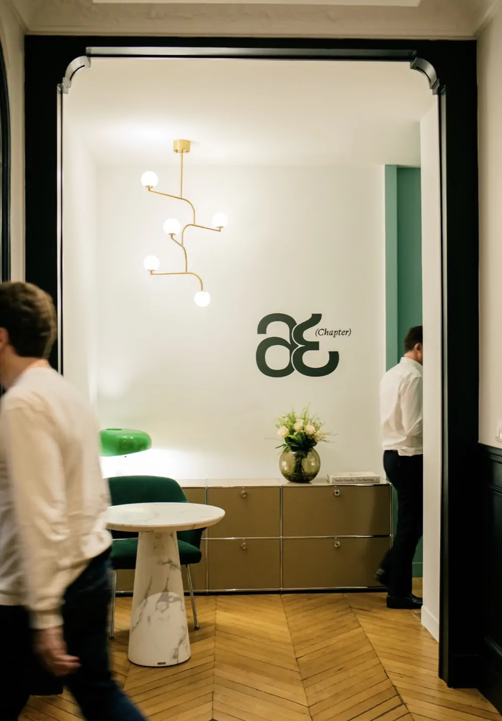 Chapter Avocats — le monogramme « æ (Chapter) » sur le mur blanc d’un bureau, au fond d’un couloir parqueté