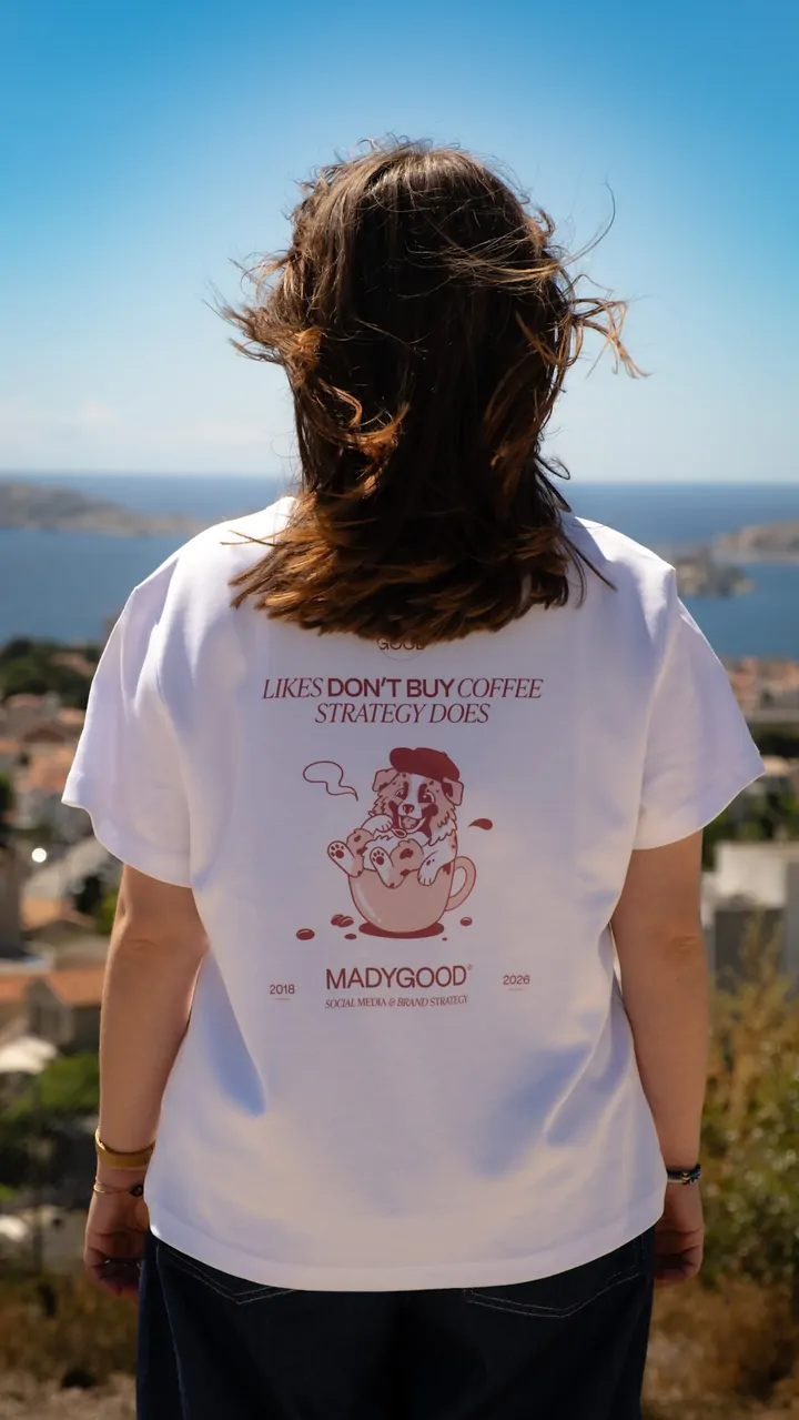 Une femme aux cheveux bouclés vue de dos, en tee-shirt blanc, face à la mer, le vent dans les cheveux.