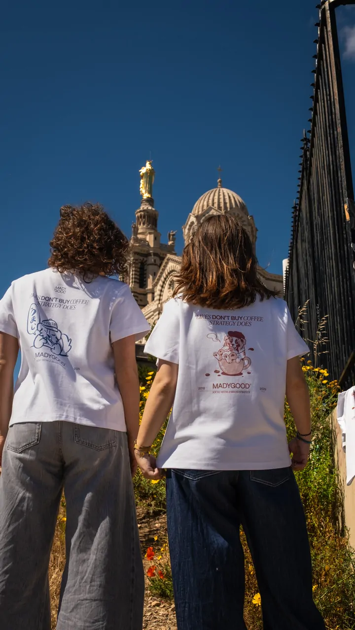 Deux personnes de dos, en tee-shirts blancs, face à la basilique et à sa statue dorée, au milieu des fleurs jaunes.