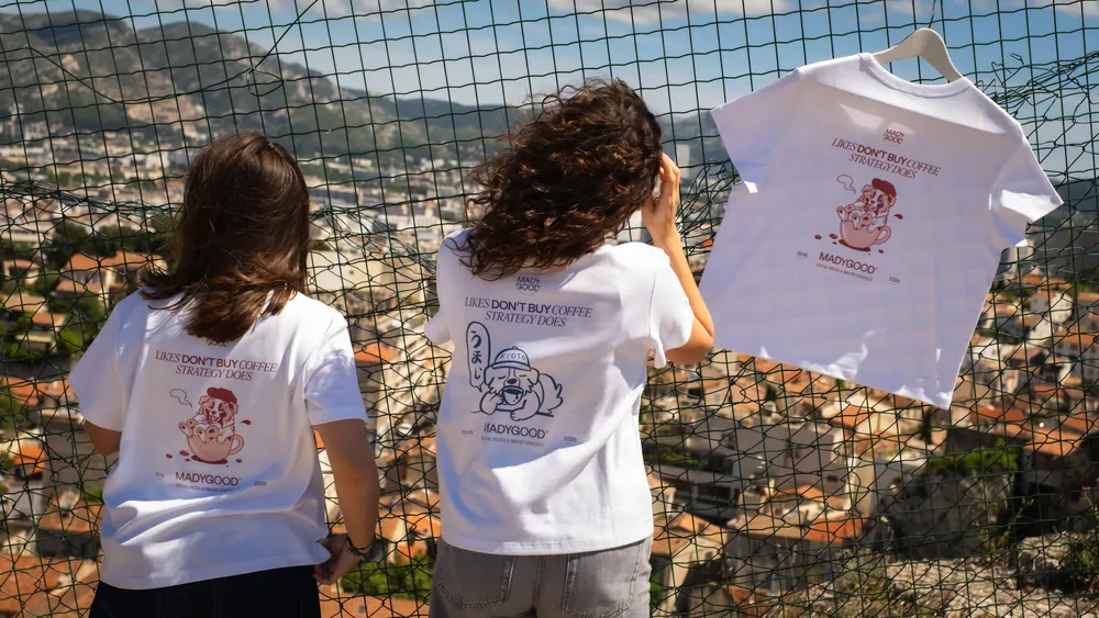 Deux personnes de dos regardent Marseille à travers un grillage, un tee-shirt suspendu à côté d’elles.